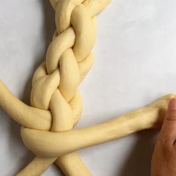 Image showing a hand braiding a 4-strand challah loaf.