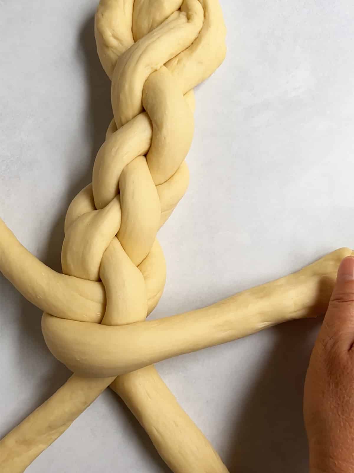 Braiding challah with 4 strands with one hand showing on the right.
