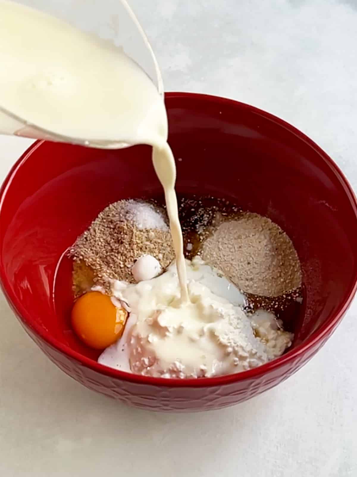 Milk pouring into a red bowl that contains all of the cottage cheese pancake ingredients.