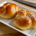 Side view at an angle of challah rolls on a white plate.