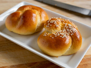 Side view at an angle of challah rolls on a white plate.