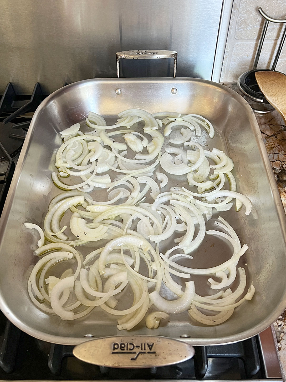 Roasting pan with onions cooking on the stove top.