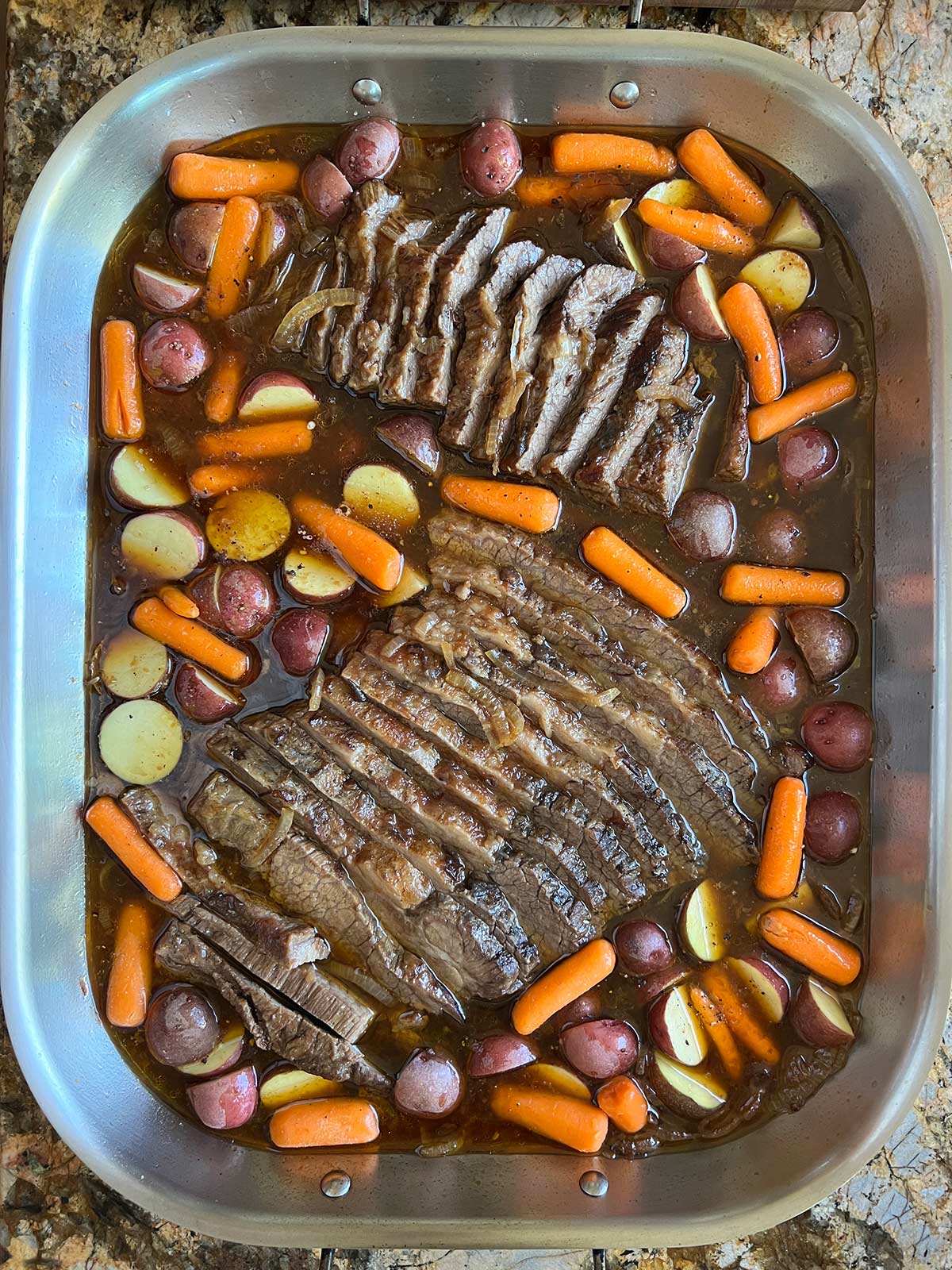 Sliced brisket placed back in pan with potatoes and carrots added in.