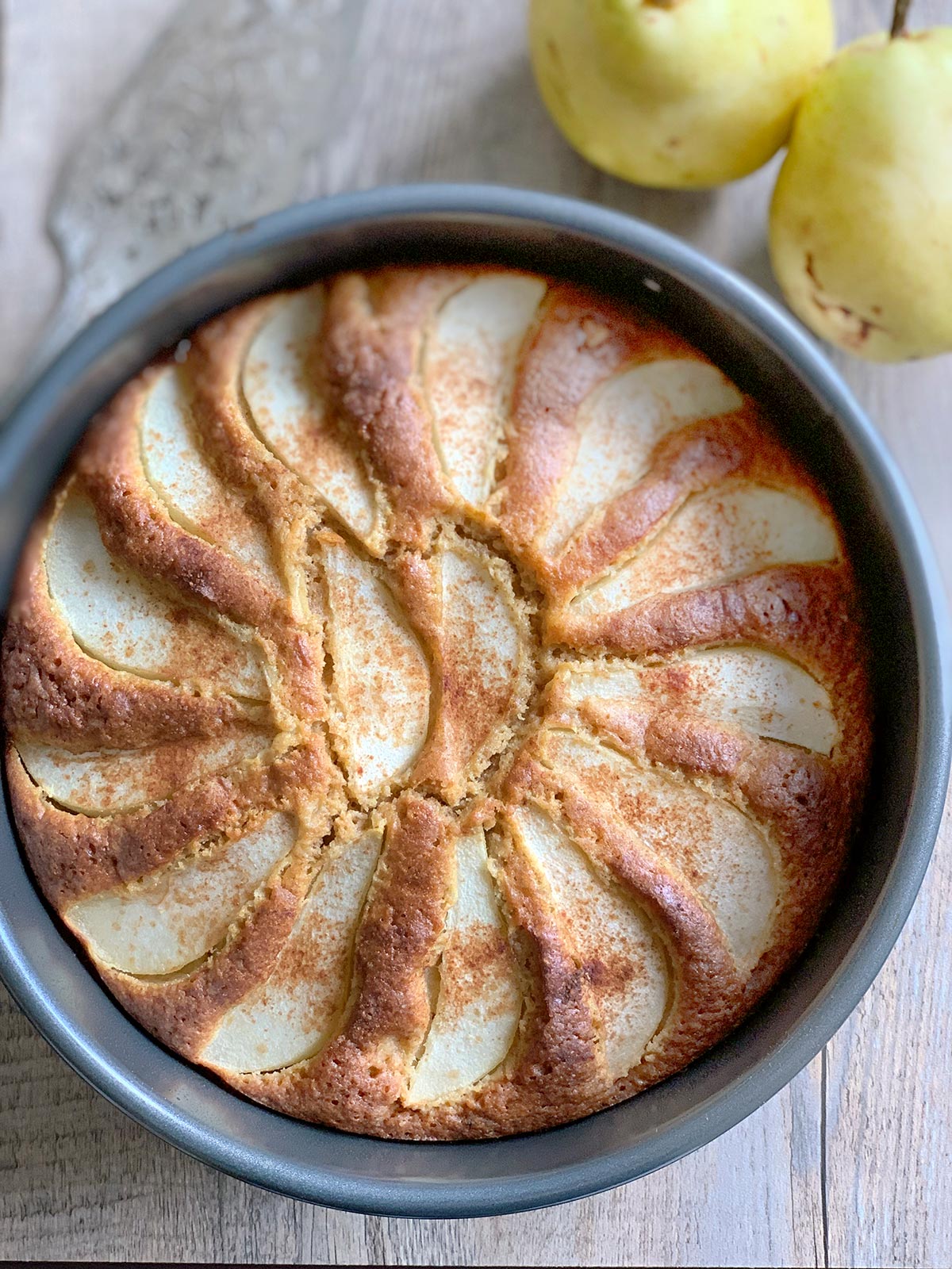 Pear cake still in baking pan with some whole pears on the side.