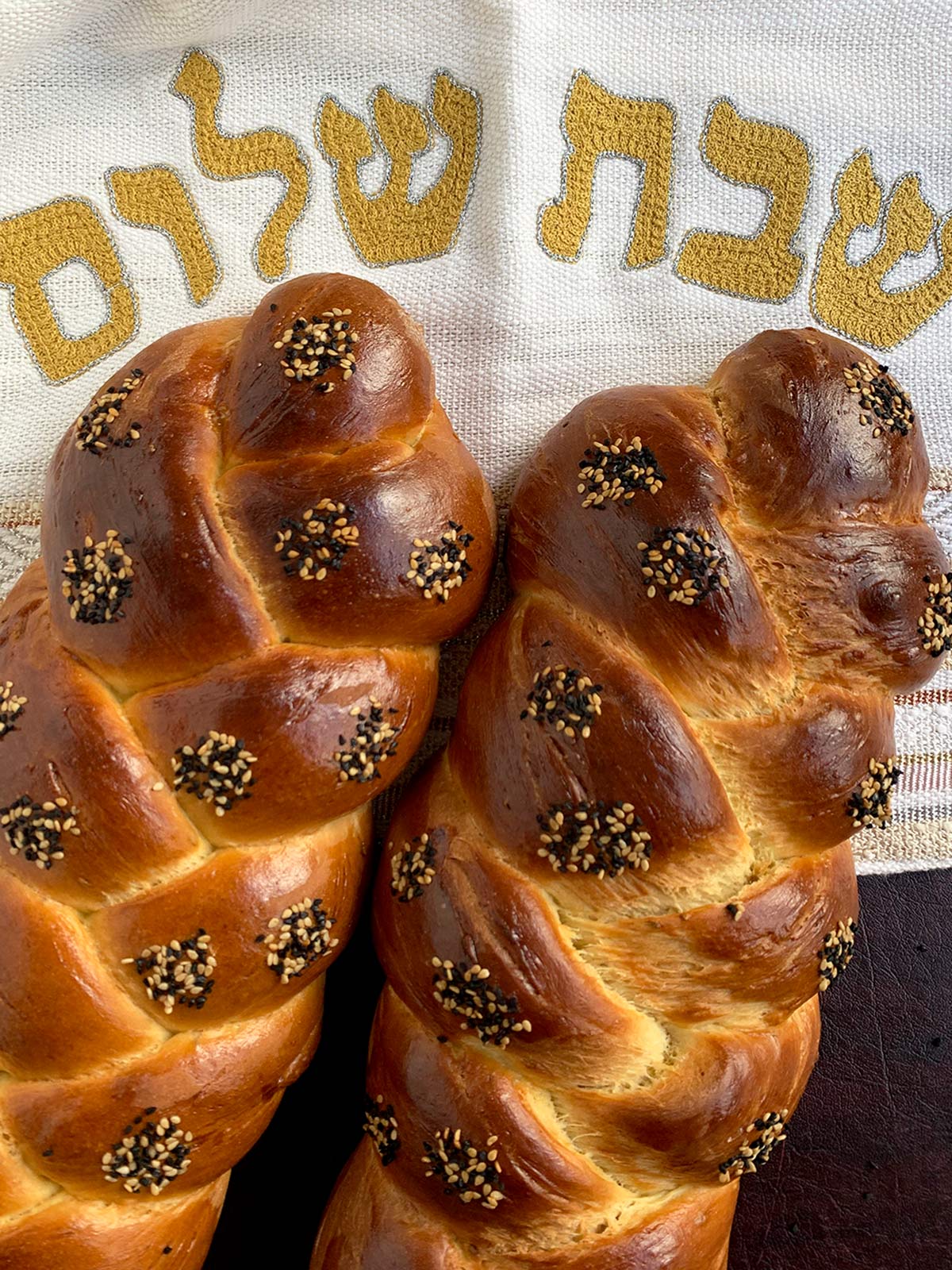 Two 3-strand challahs side by side near a challah cover.