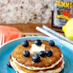 Stack of pancakes on a blue plate with blueberries and butter on top.