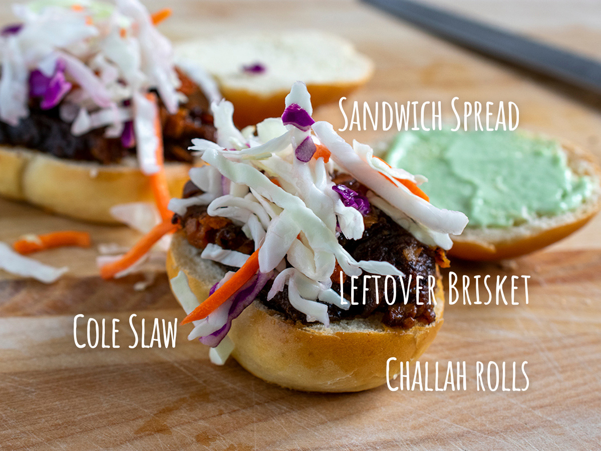 Close up of one of the open-faced sandwiches with labels on the sandwich spread, brisket, rolls and cole slaw.