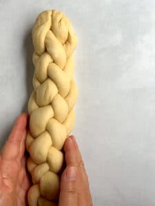 Finished 6-strand challah braid with two hands adjusting it.