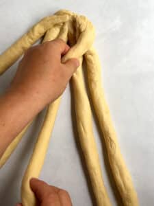 Demonstrating bringing the outside strand over 2 for a 6-strand challah braid.