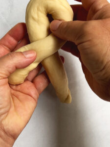 Demonstrating a challah roll knot, we see the first crossover of the strand.