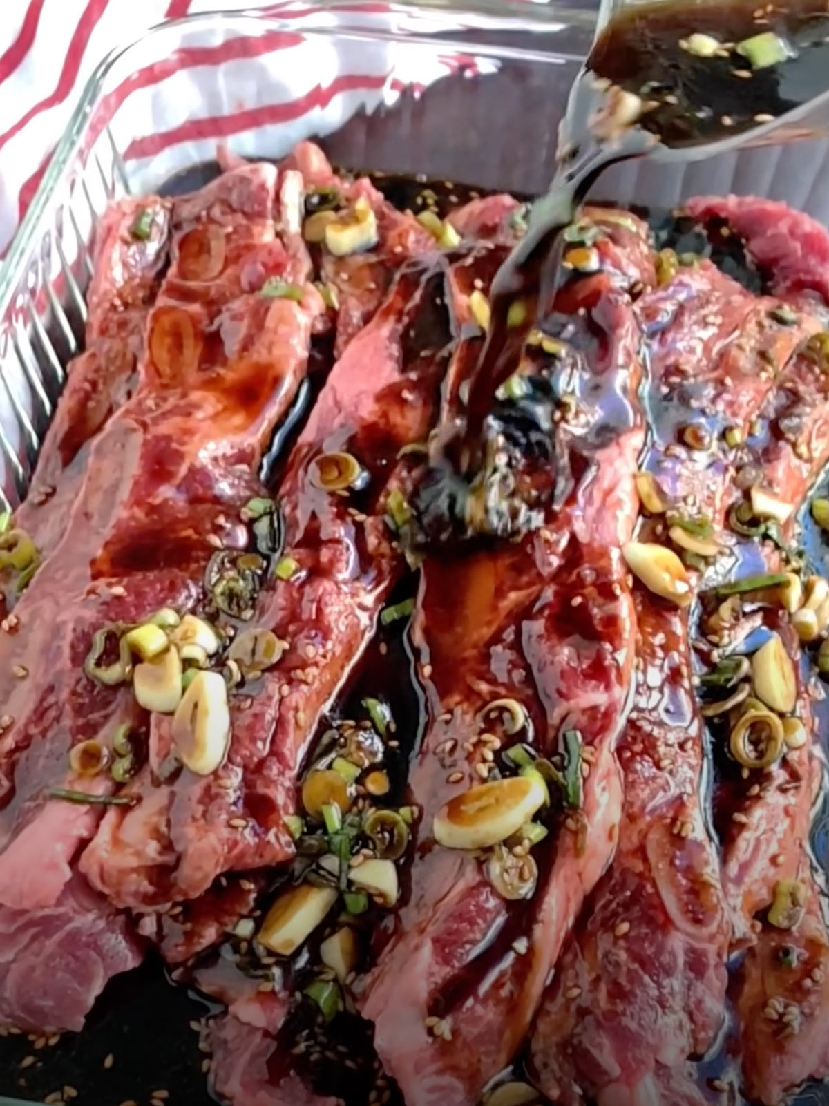 Kalbi marinade pouring over ribs from a measuring cup.