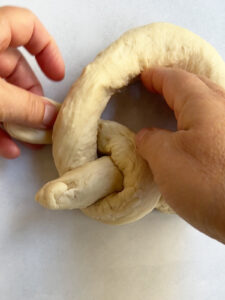 Step 3 of single strand challah braid showing the leg of the key going further into the circle.