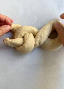 Step 5 of single strand challah braid showing the resulting shape of the circle formed from the twist.