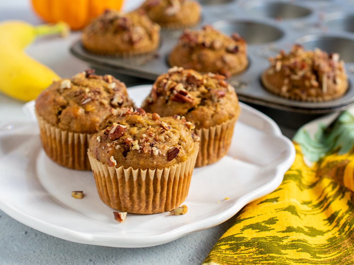 Landscape beauty shot of muffins on a pumpkin shaped plate with the whole muffin baking tin in the background.
