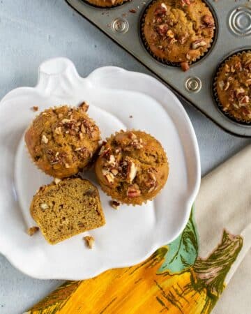 Pumpkin banana muffins on a pumpkin shaped plate with a muffin tin of muffins next to it.