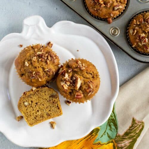 Pumpkin banana muffins on a pumpkin shaped plate with a muffin tin of muffins next to it.
