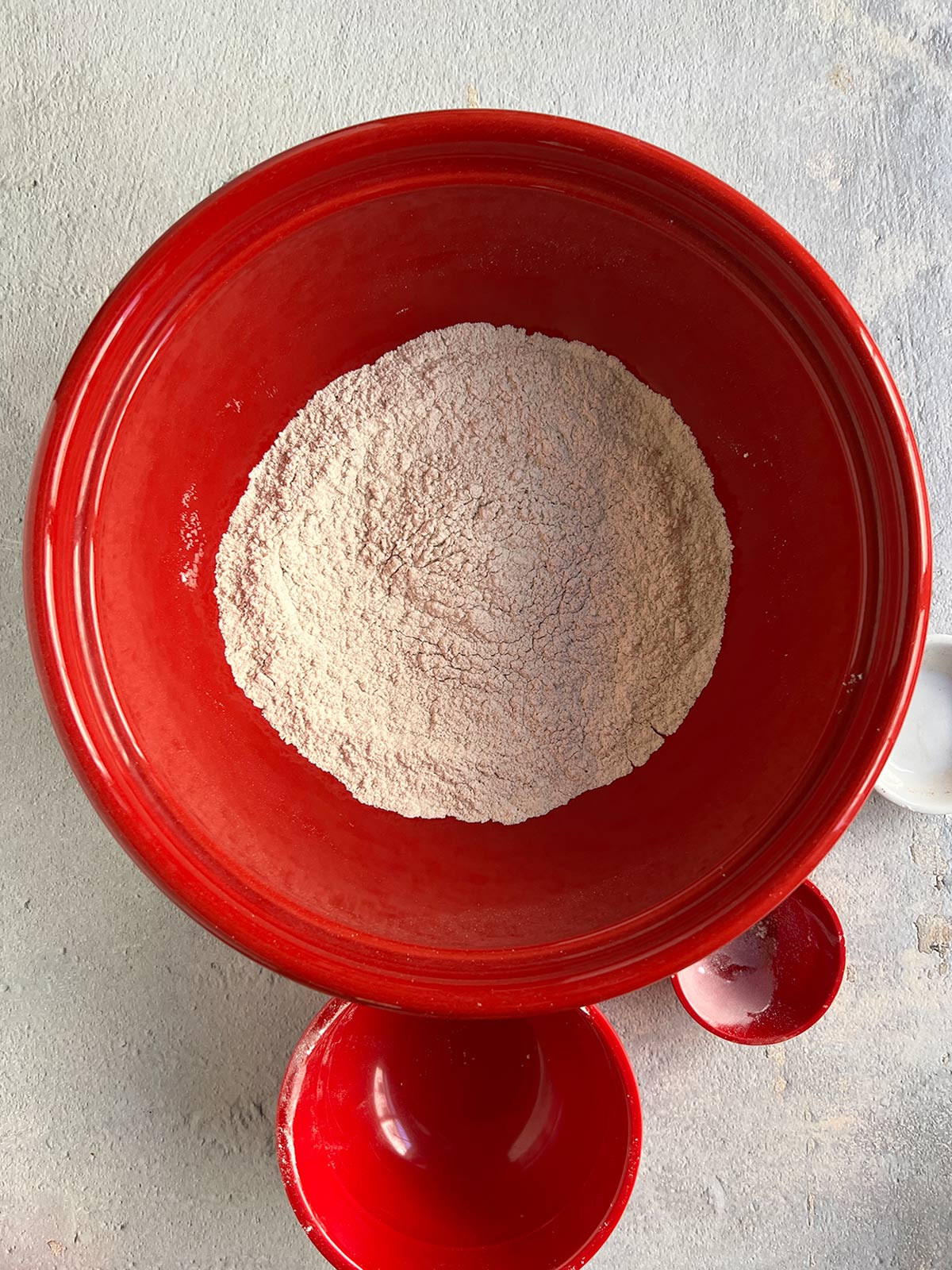 Dry ingredients whisked in a big red bowl with small bowls around it.