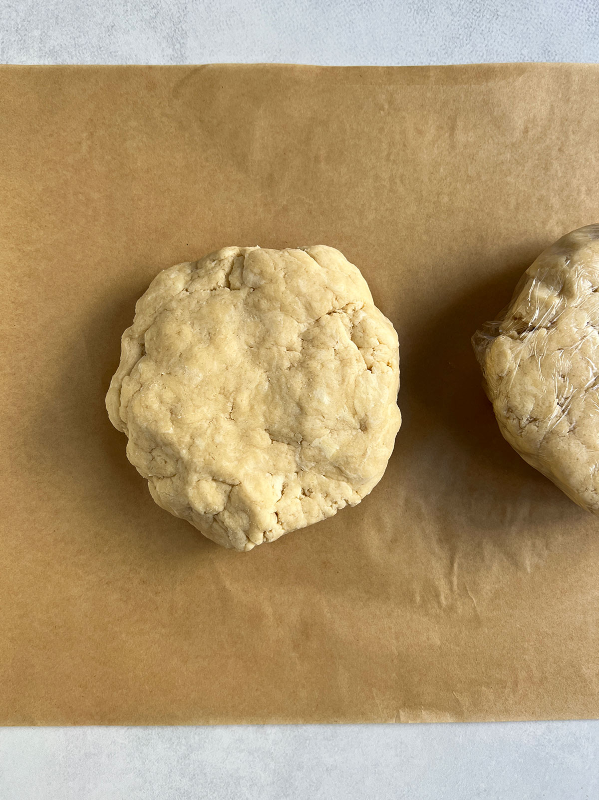 Disk of pie dough on parchment with a wrapped disk to the side partially showing.