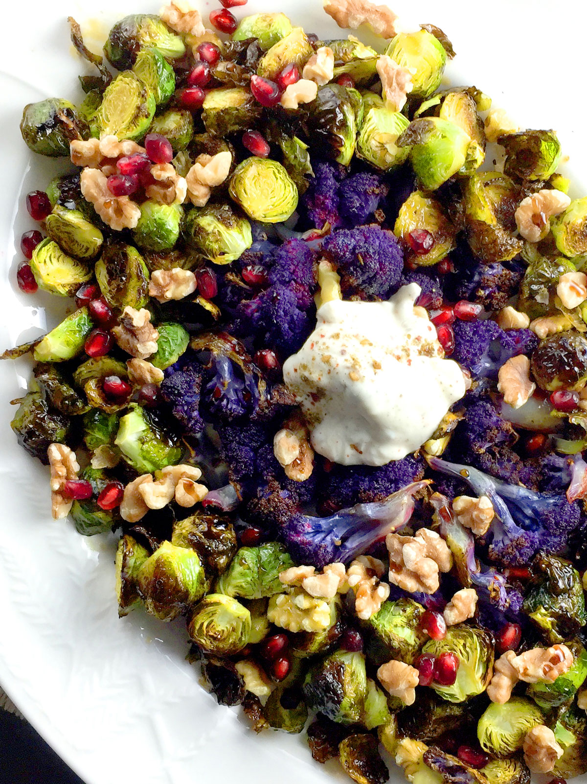 Brussels and cauliflower on a white plate with a yogurt sauce in the center.