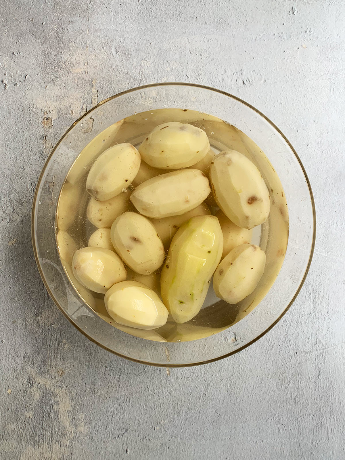 Peeled potatoes in a clear bowl in water.