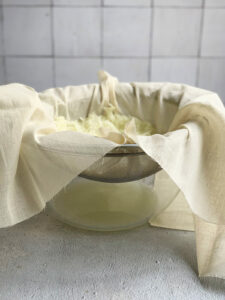 Strainer and cheesecloth suspended in a large glass bowl.