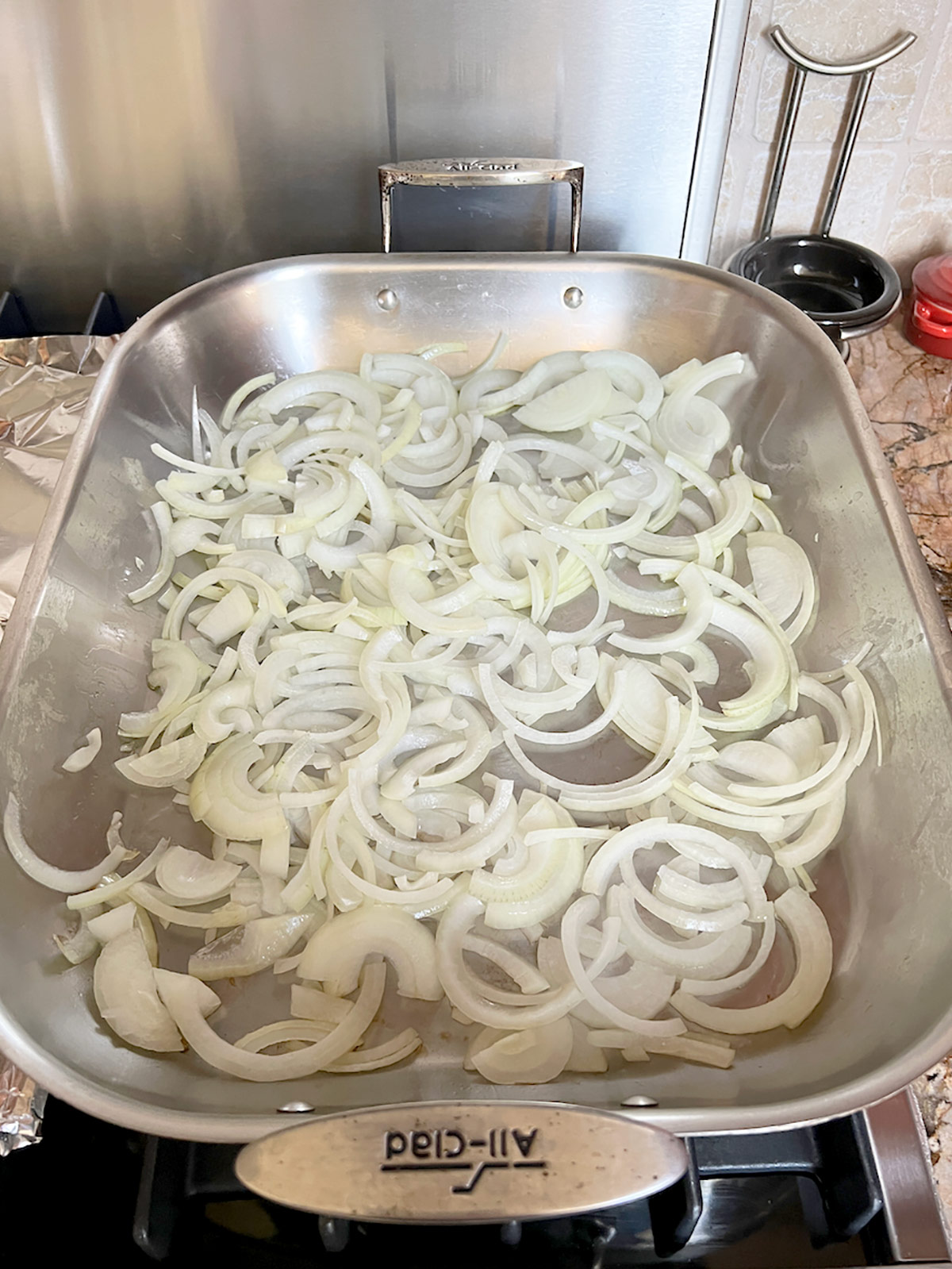 Onions browning in a large roasting pan on the stove top.