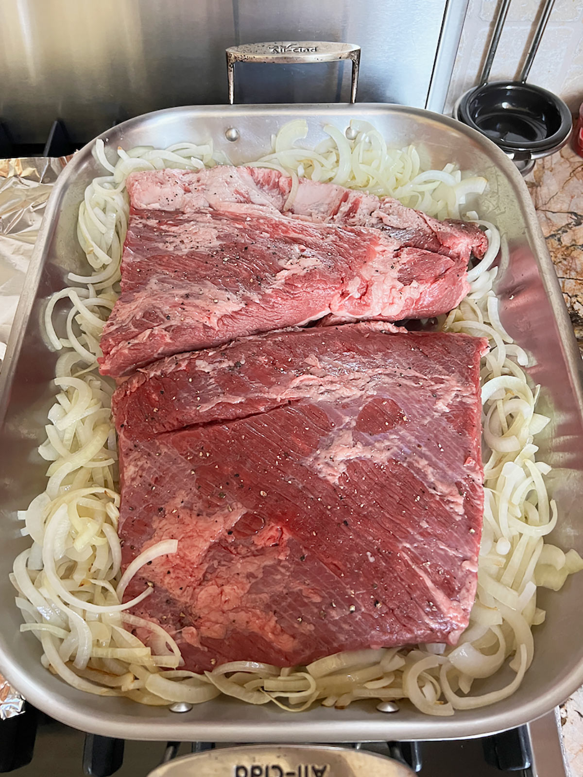 Brisket placed in large roasting pan with the onions pushed to the side.