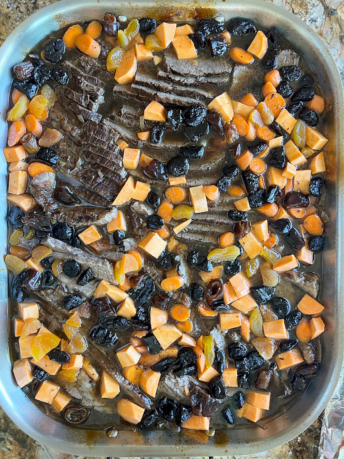 Vegetables and dried fruit added to braised beef brisket and ready to go back in the oven.