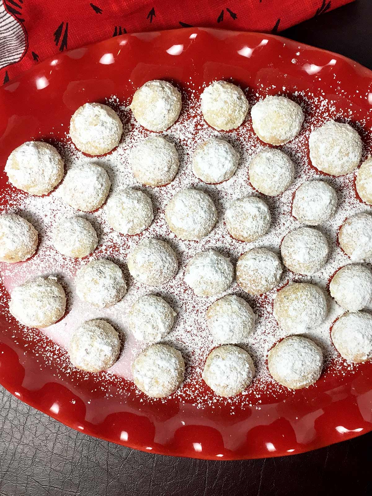 Pistachio snowballs on a red platter with second dusting of powdered sugar on them.
