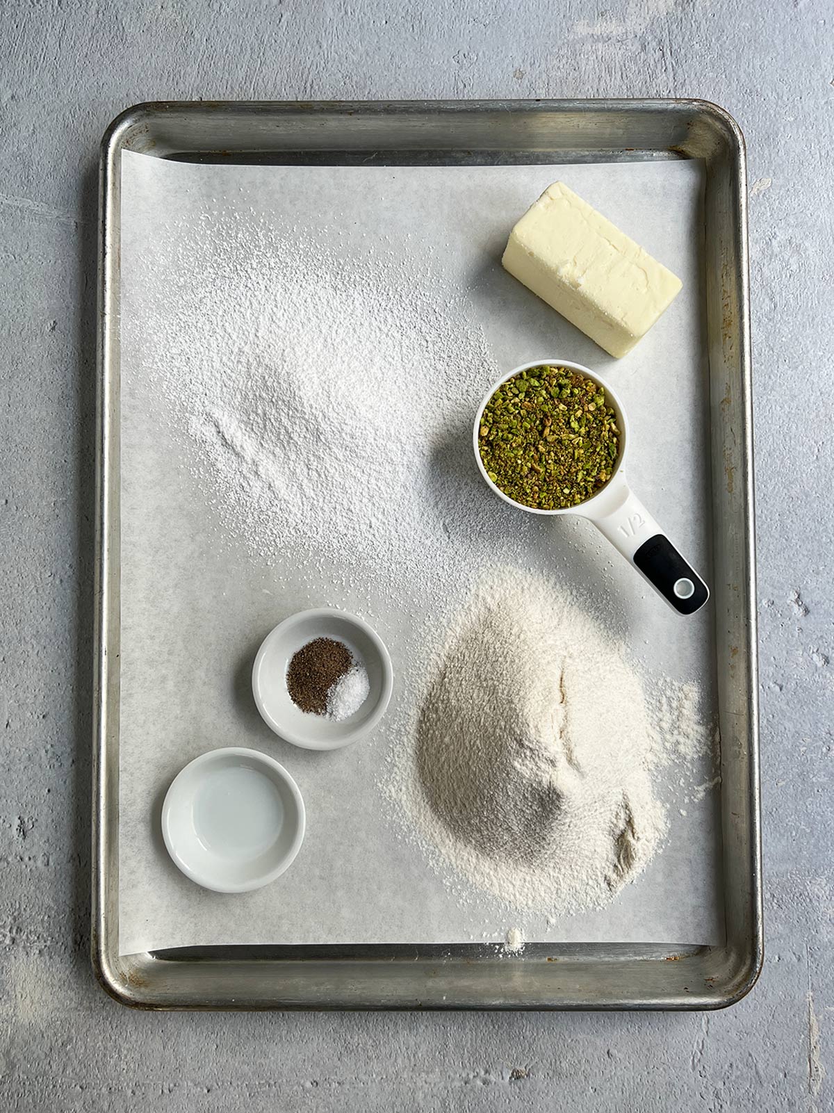 Pistachio snowball ingredient shot showing sifted flour and sugar on parchment. 