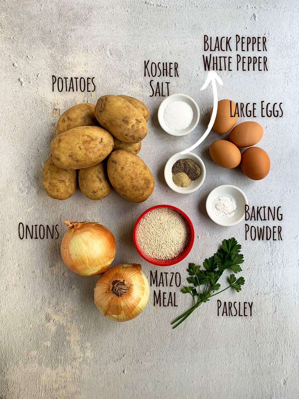 Ingredient shot for crispy potato pancakes showing potatoes, onions, matzo meal, eggs, spices and parsley.