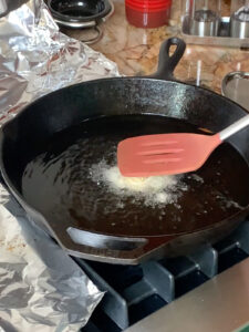 Red spatula smashing a potato latke in cast iron pan.