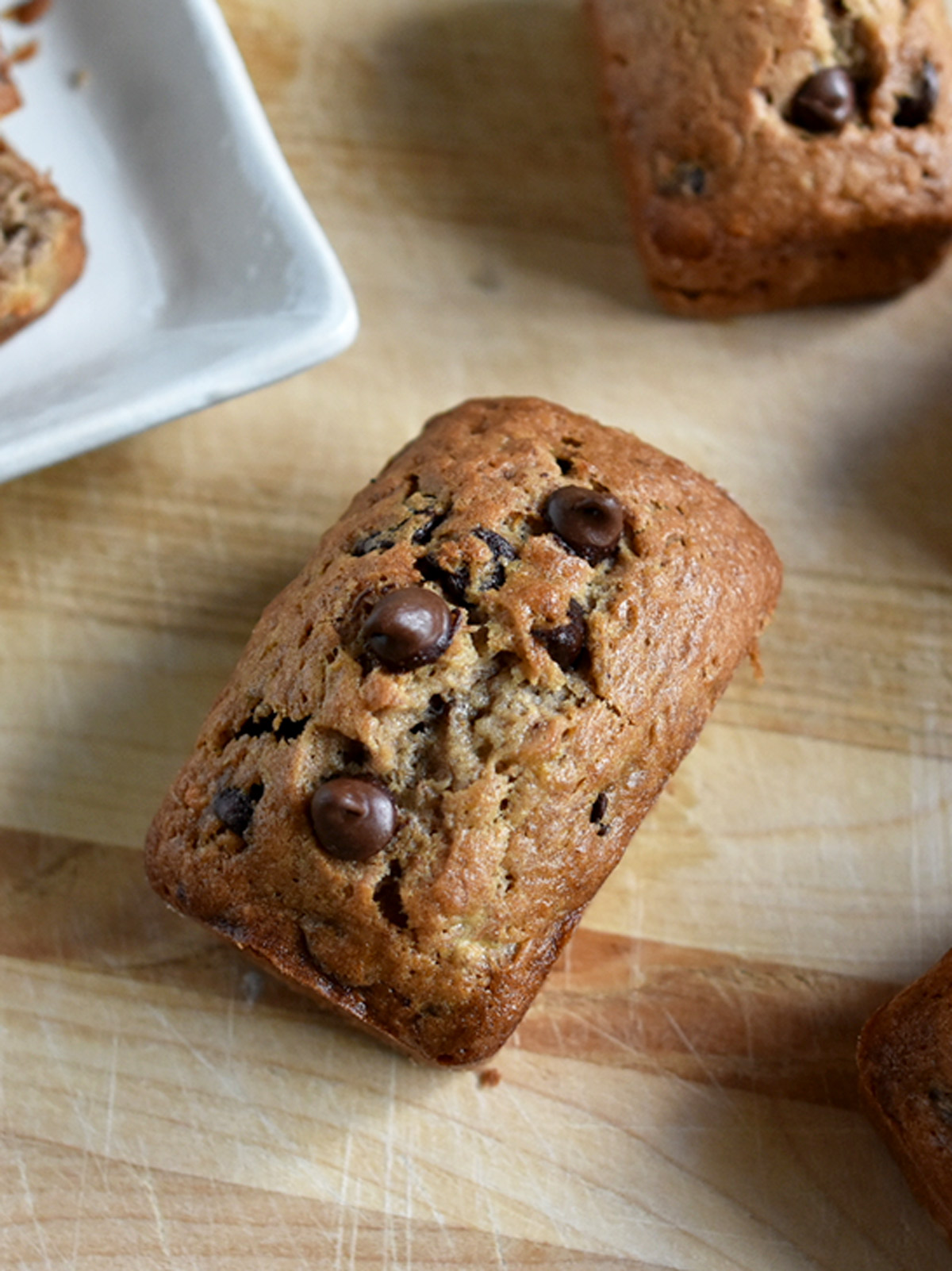 One mini banana chocolate chip loaf on a wooden board.