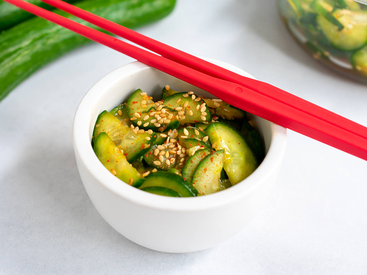 Korean pickled cucumbers in a white bowl with red chopsticks.