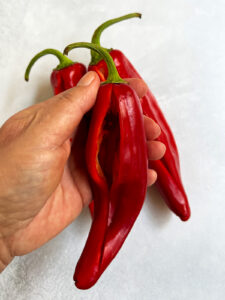 Hand holding a romano pepper that has been slit open.