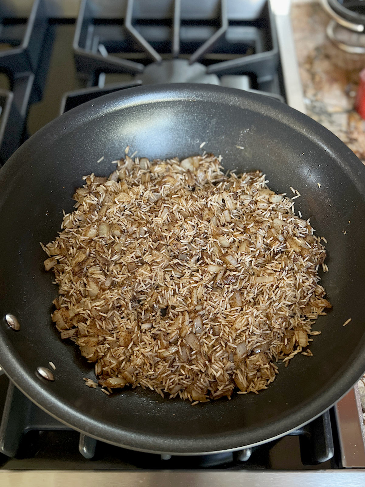 Onions, rice, and spices all mixed together in the fry pan.