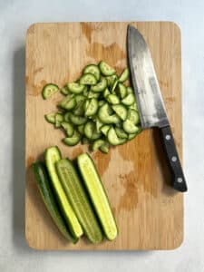 Cutting cucumbers for Korean cucumber salad on a wooden cutting board with a Japanese knife.
