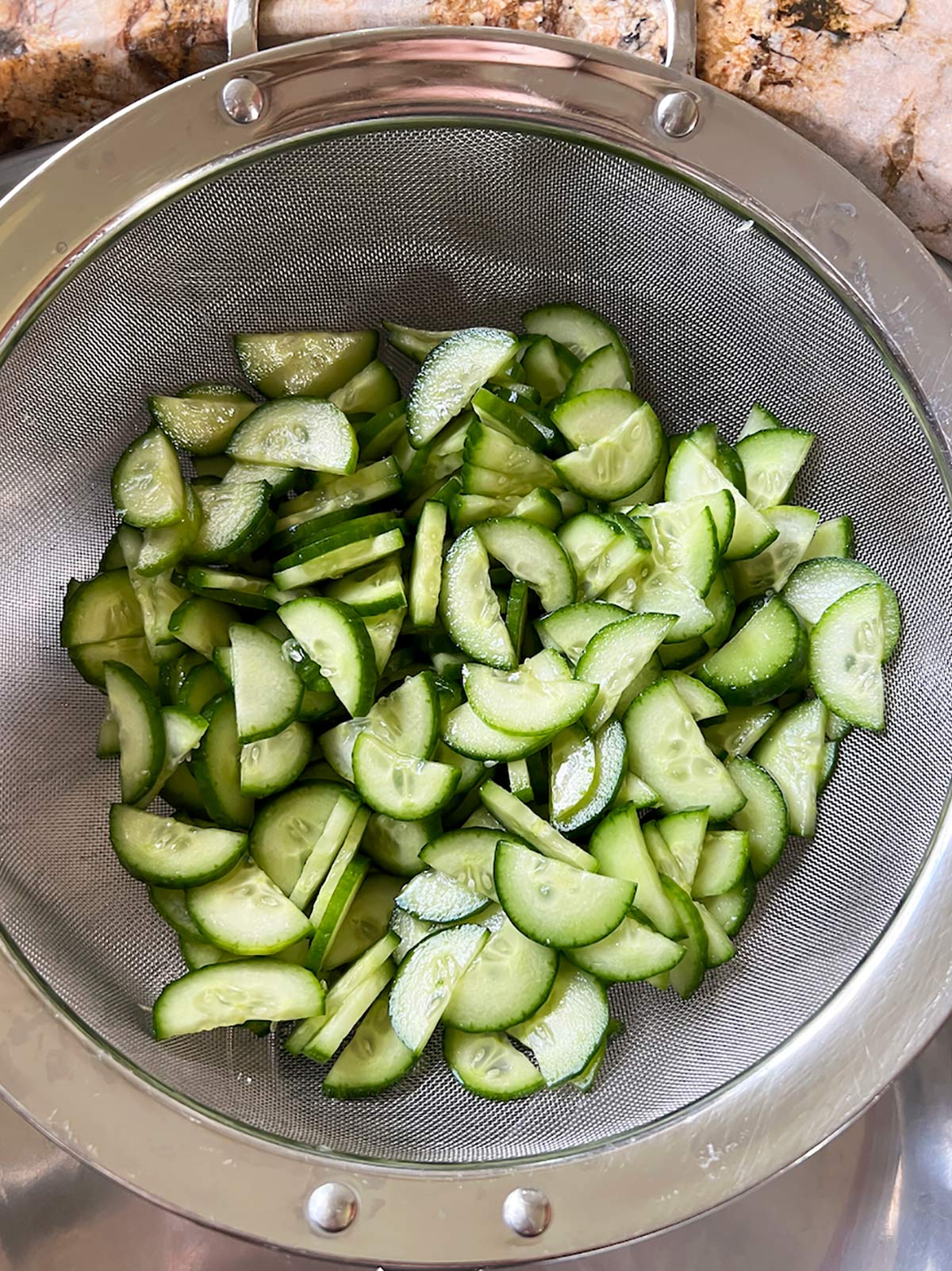Sliced cucumbers in a strainer over a sink.