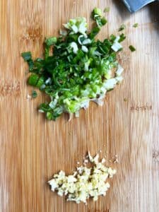 Finely chopped garlic and green onions on a wooden cutting board.