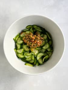 Seasoning mixture poured on cucumbers in white bowl ready to be mixed to create the Korean cucumber salad..