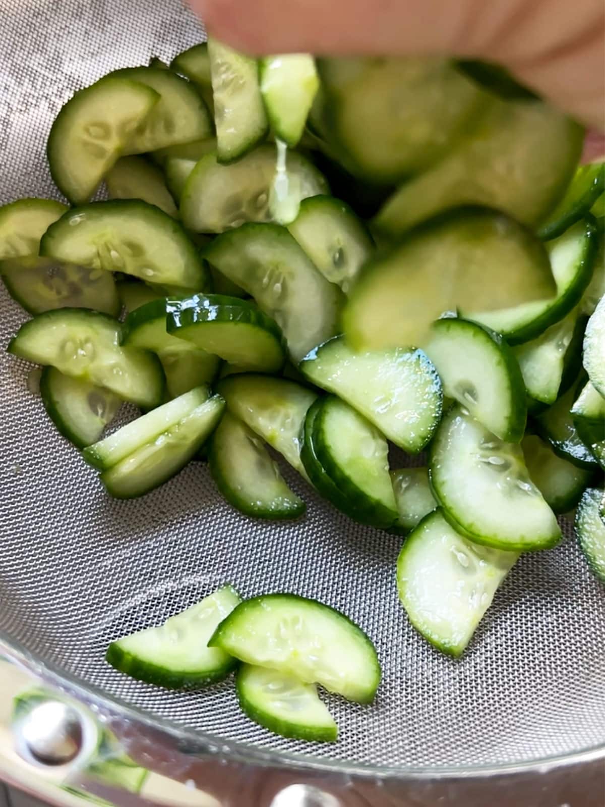 Squeezing water out of cucumbers over a strainer.