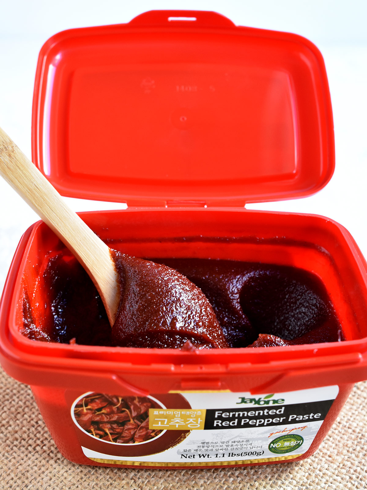 Gochujang on a wooden spoon in a red container.