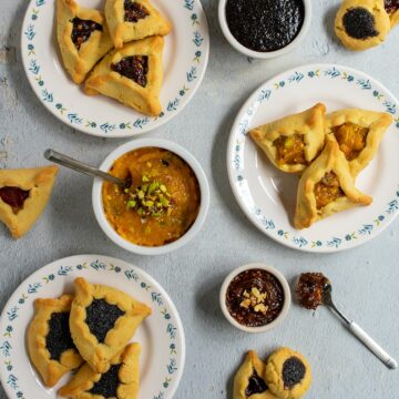 Three kinds of hamantaschen on flowery white plates with their associated fillings nearby.