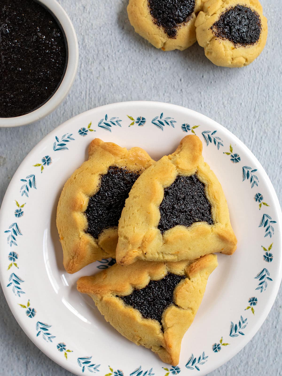 Hamantaschen filled with poppy seed filling and a bowl of poppy seed filling.