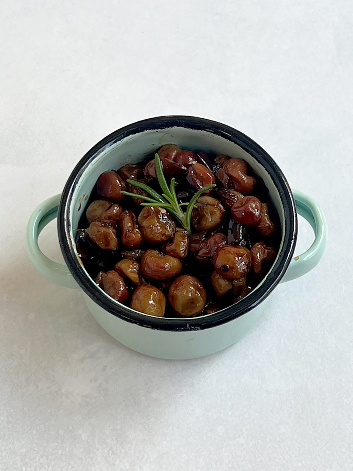 Roasted grapes in a turquoise serving bowl with rosemary on top.
