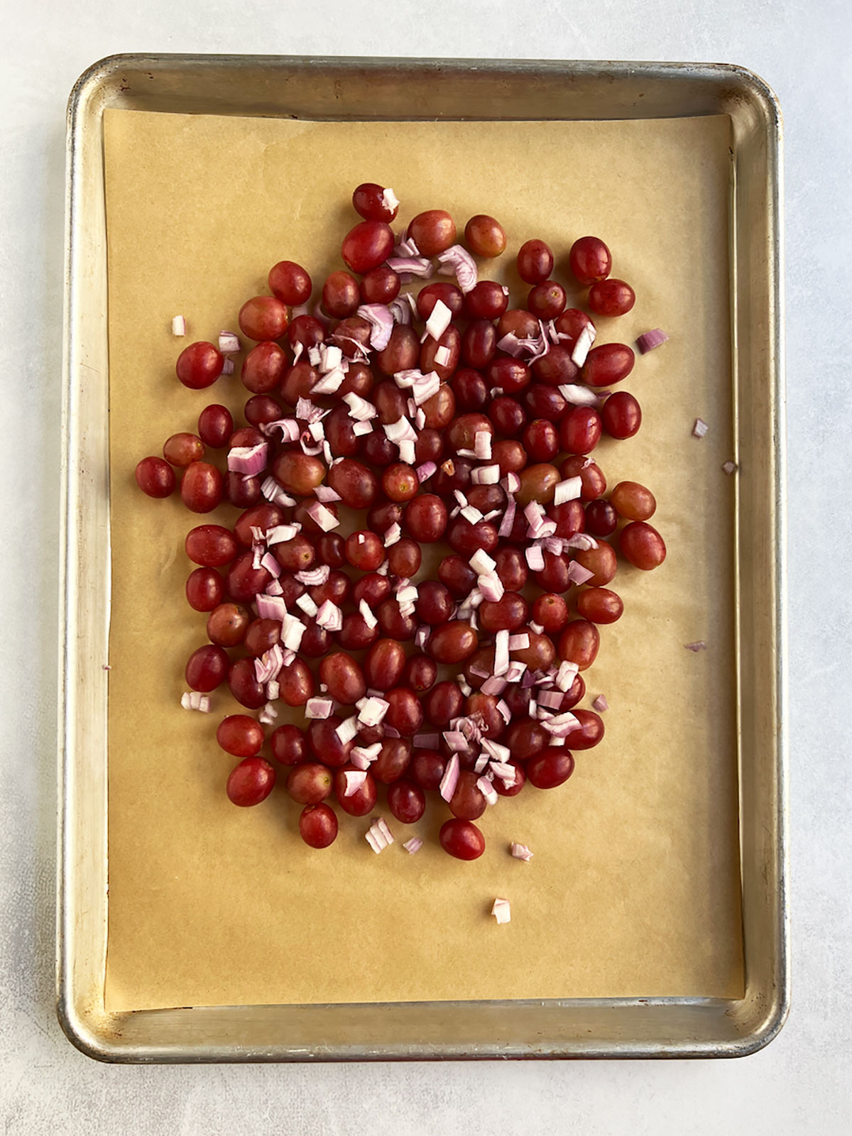 Uncooked grapes and shallots on a parchment-lined baking sheet.