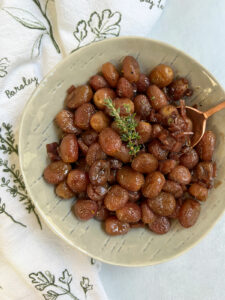 Roasted grapes in a grey bowl with an herby napkin and copper spoon.