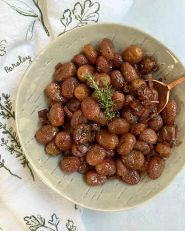 Roasted grapes in a grey bowl with an herby napkin and copper spoon.