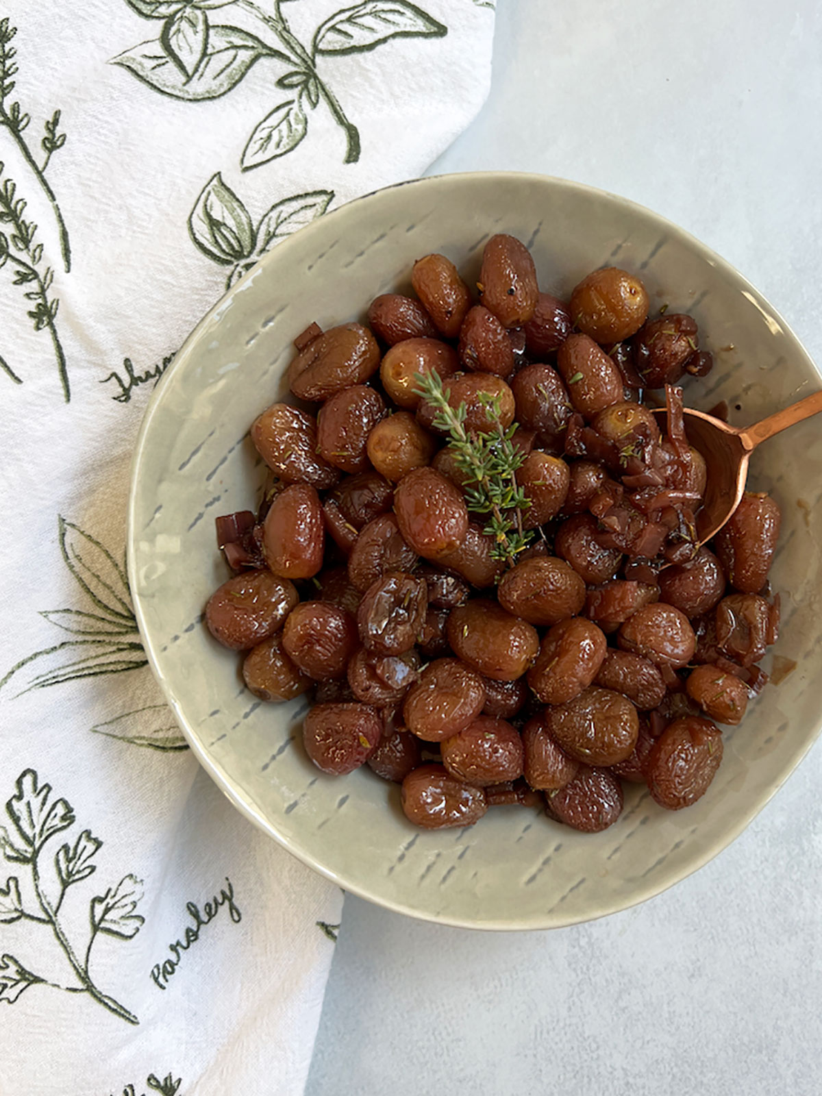 Roasted grapes in a bowl with a copper spoon.
