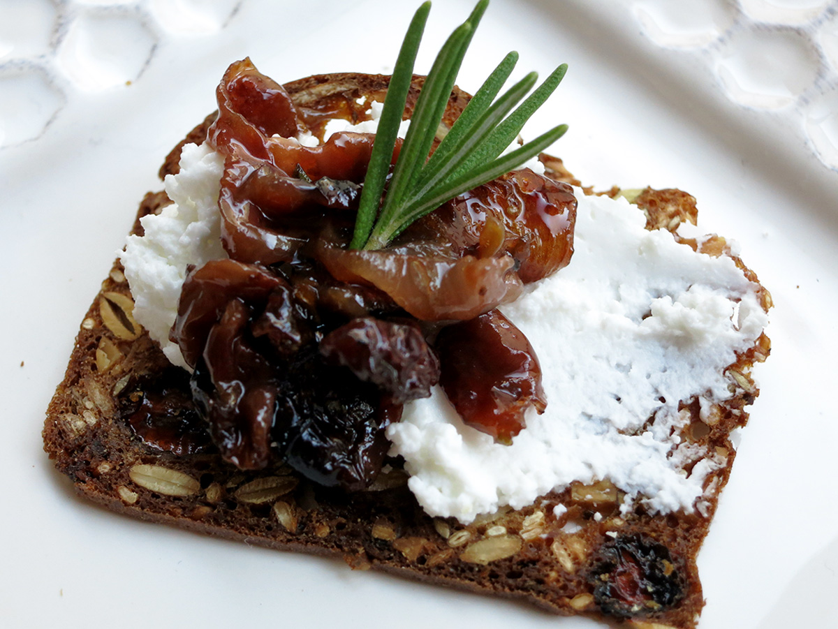 Roasted grapes and goat cheese on a fig cracker with a sprig of rosemary on top.